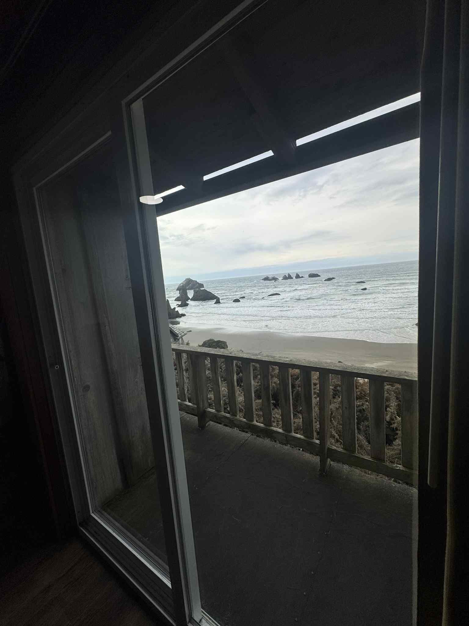 Vista desde el interior de un edificio hacia una playa con rocas y una barandilla de madera.