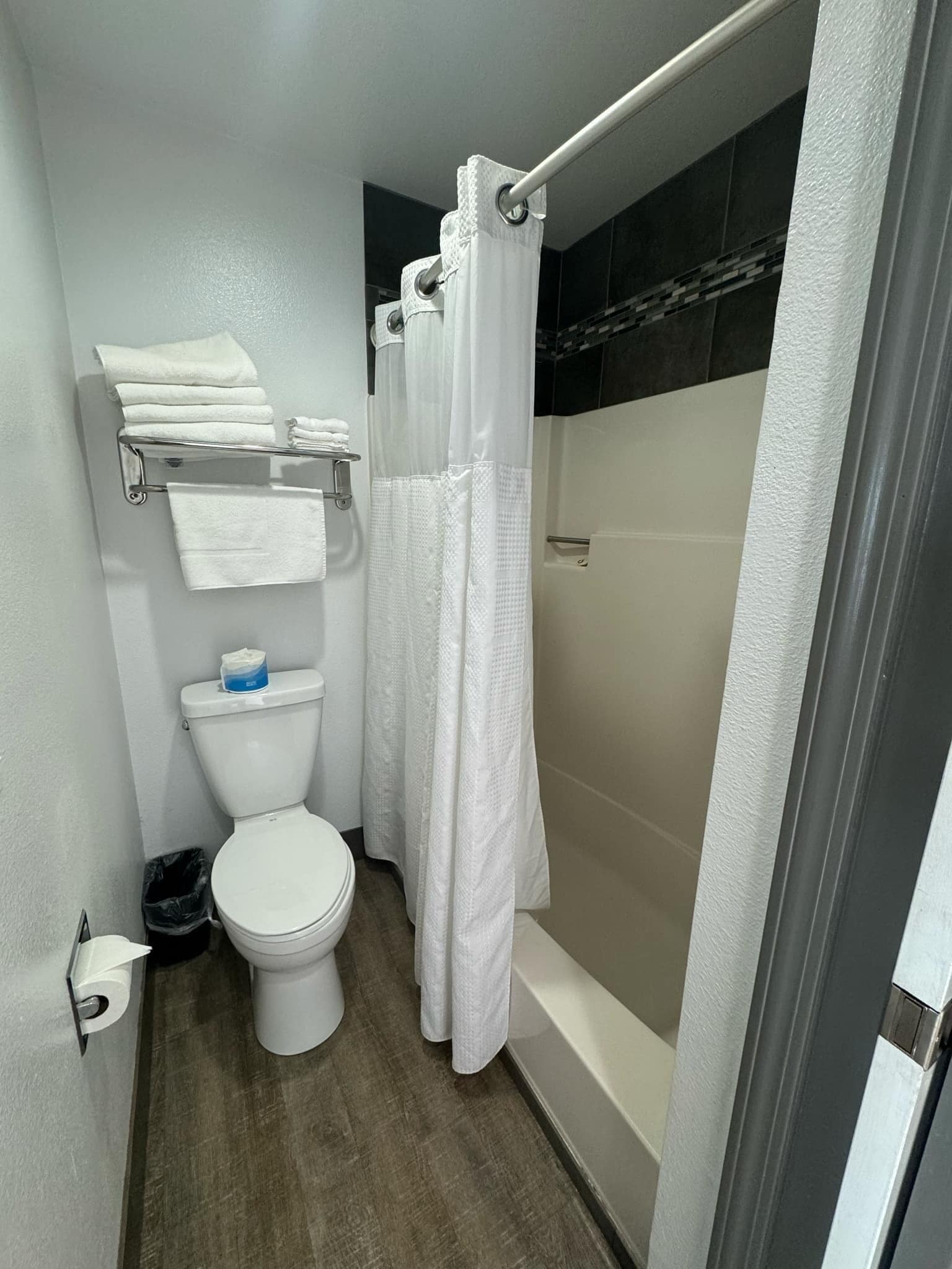 A small, modern bathroom with a toilet, a shower with a white curtain, and a towel rack with folded towels.