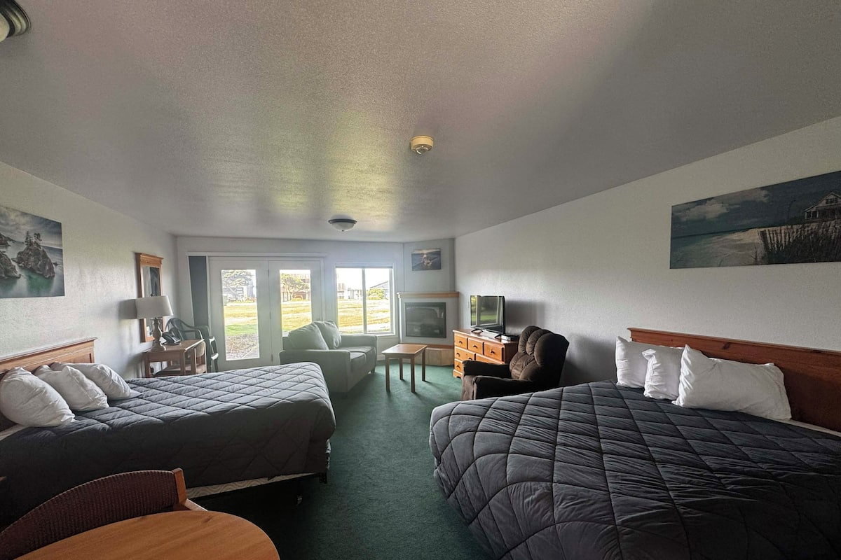 A hotel room with two beds, a desk, a chair, a television, and a fireplace.