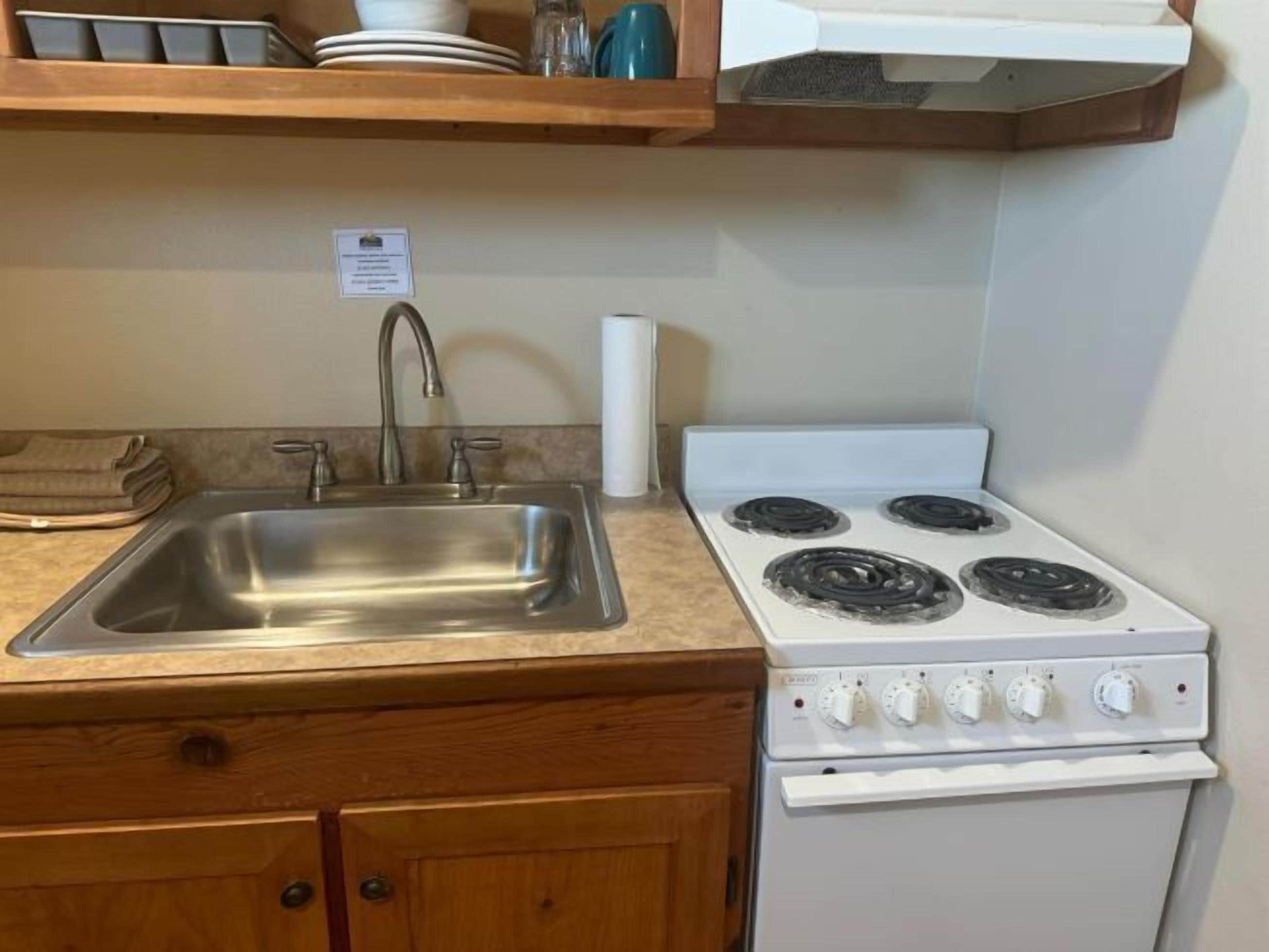 A kitchen with a stainless steel sink, a white stove with four burners, wooden cabinets, and a wooden countertop.