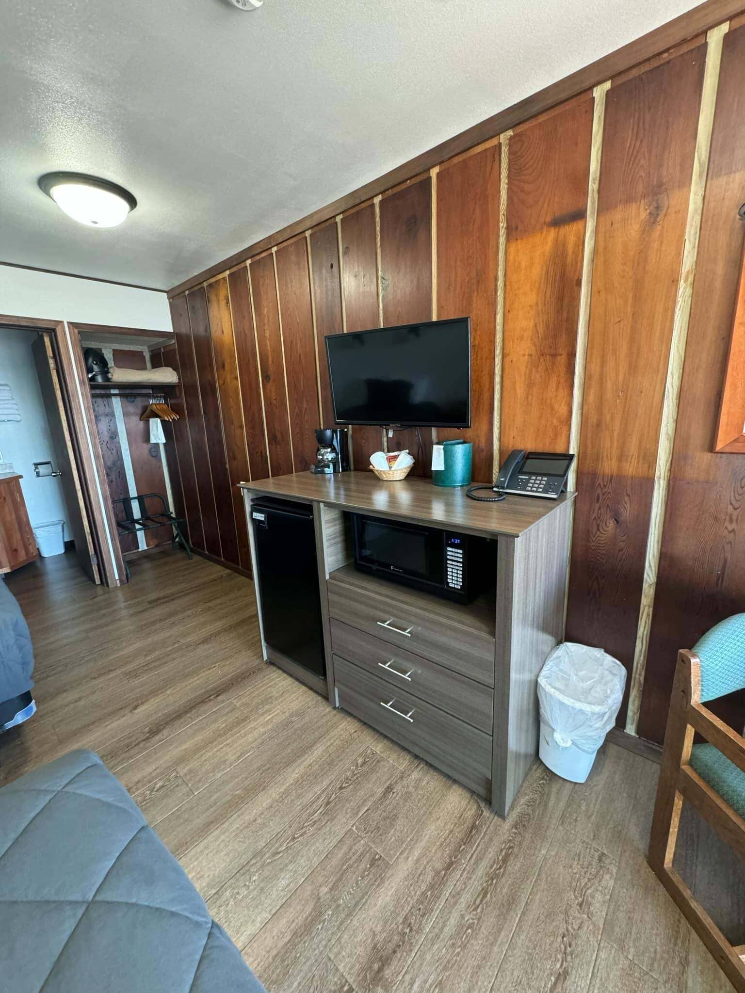 A compact kitchenette with wooden paneling, a built-in microwave, a small refrigerator, a sink, and a flat-screen TV.