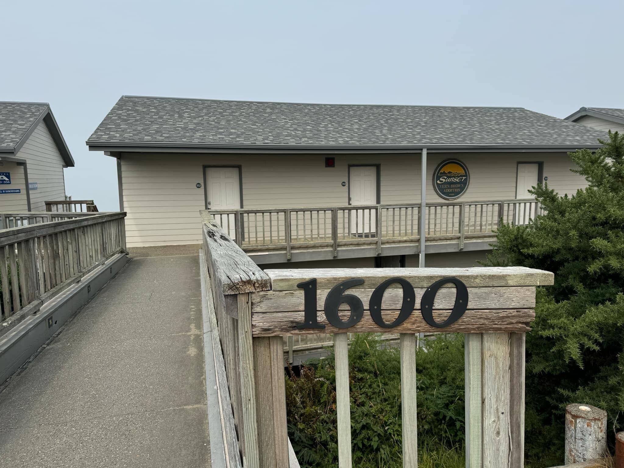 A wooden gate with the number 1600, leading to a building with a balcony and a sign that reads "Sunset Vineyard Addition".