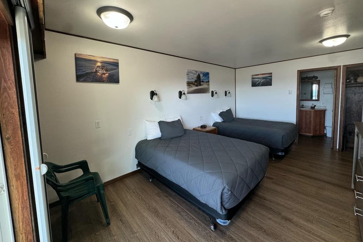 A room with two beds, a wooden floor, and a small green chair.