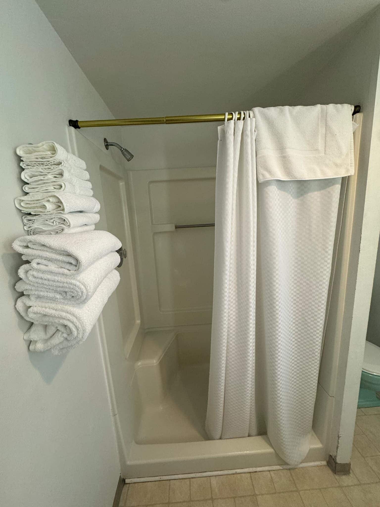 A shower area with a white shower curtain and a towel rack with folded towels.