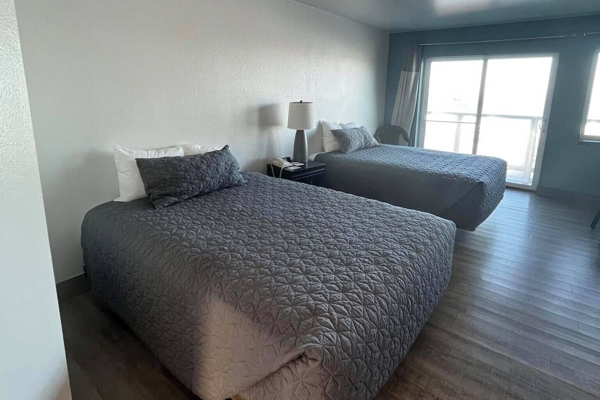 A hotel room with two beds, a nightstand, and a window with curtains.