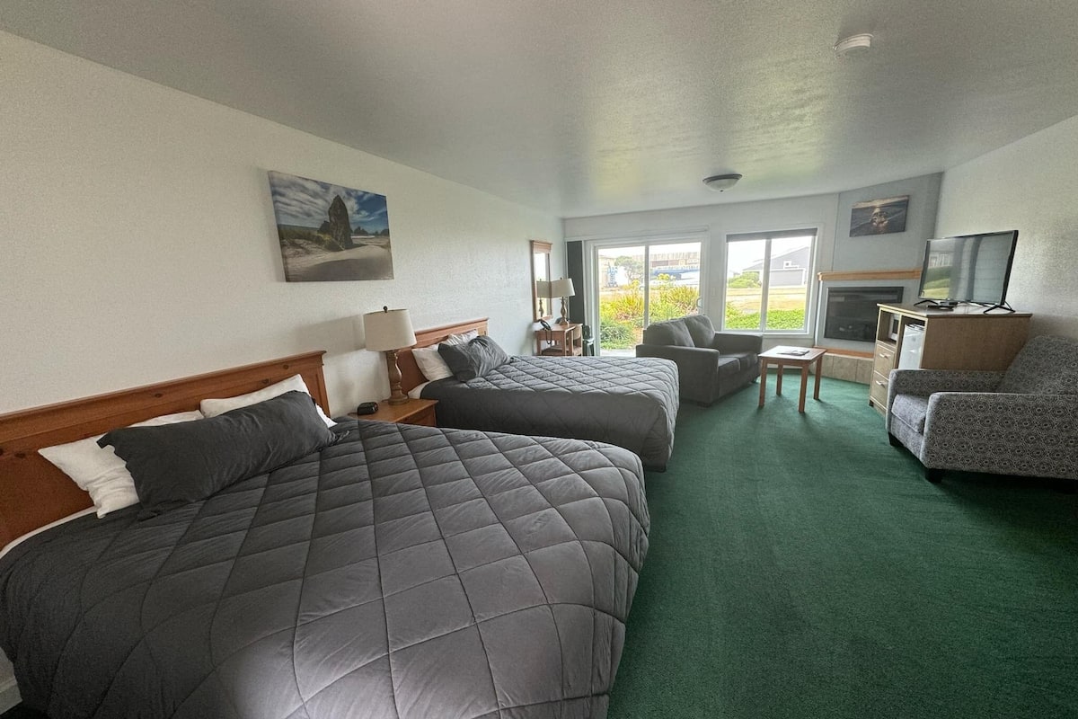 A hotel room with two beds, a sofa, a TV, and a fireplace.