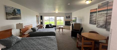 A hotel room with two beds, a desk, a TV, and a dining table.
