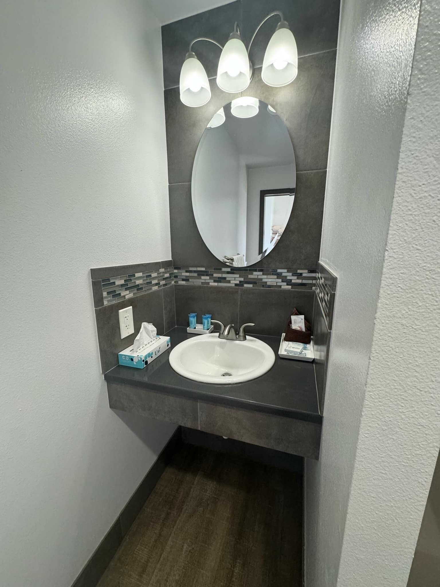 A bathroom with a white sink, a large mirror, and three wall-mounted lights.