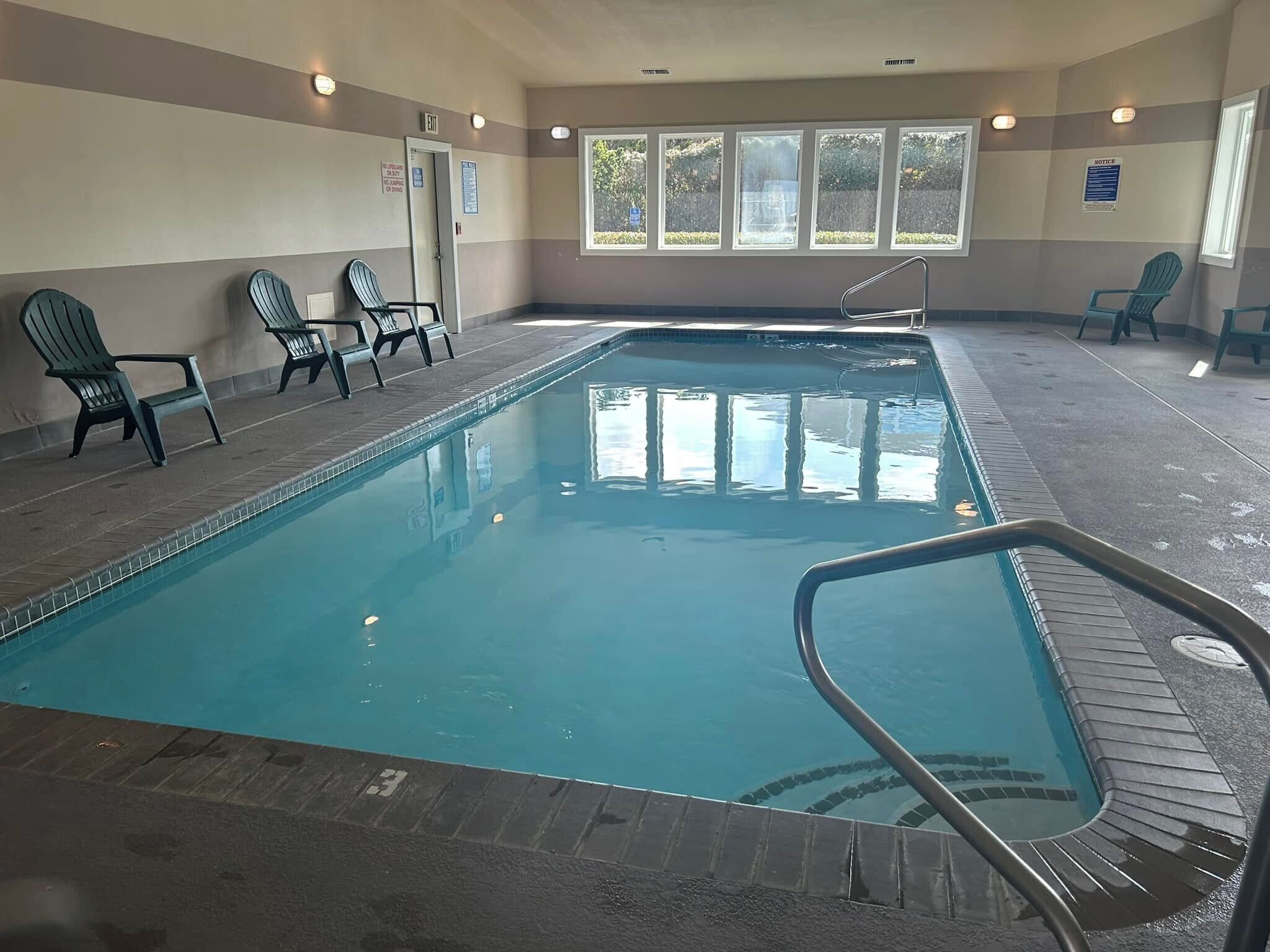 An indoor swimming pool with a clear water surface, surrounded by lounge chairs and a tiled floor.