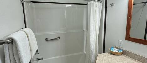 A bathroom with a glass shower enclosure, a white sink, and a wooden vanity.