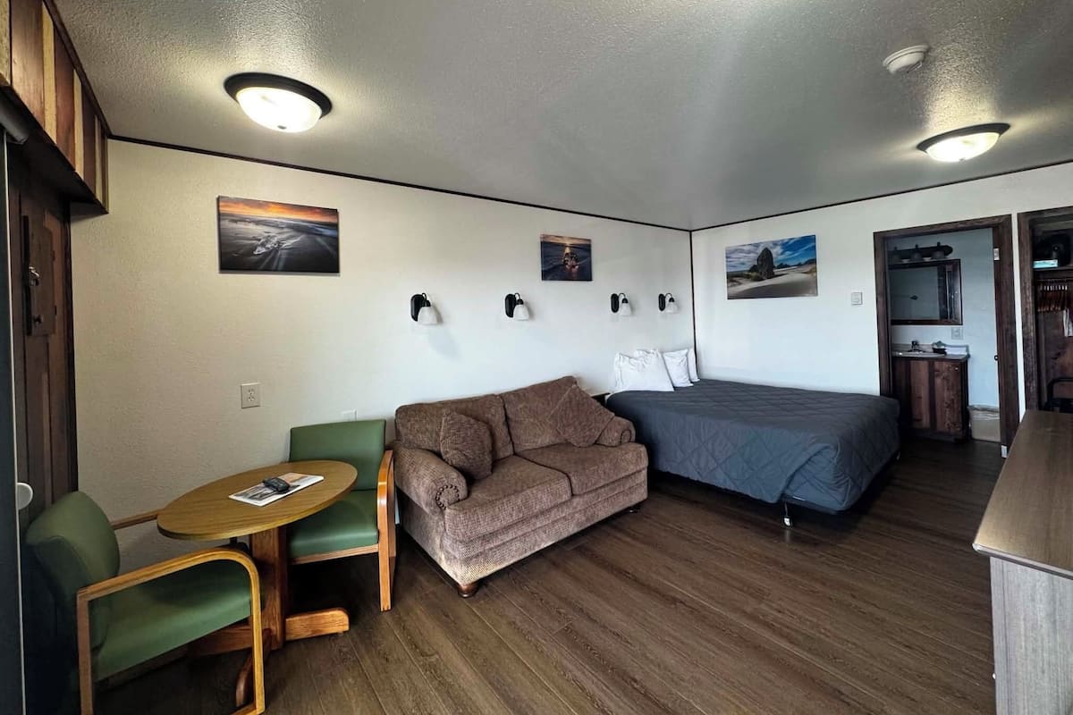 A compact room with a sofa, a small table, a bed, and a kitchenette area.