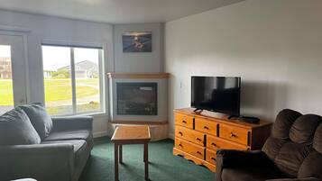 Una sala de estar con chimenea, televisión y vista a un patio verde a través de amplios ventanales.