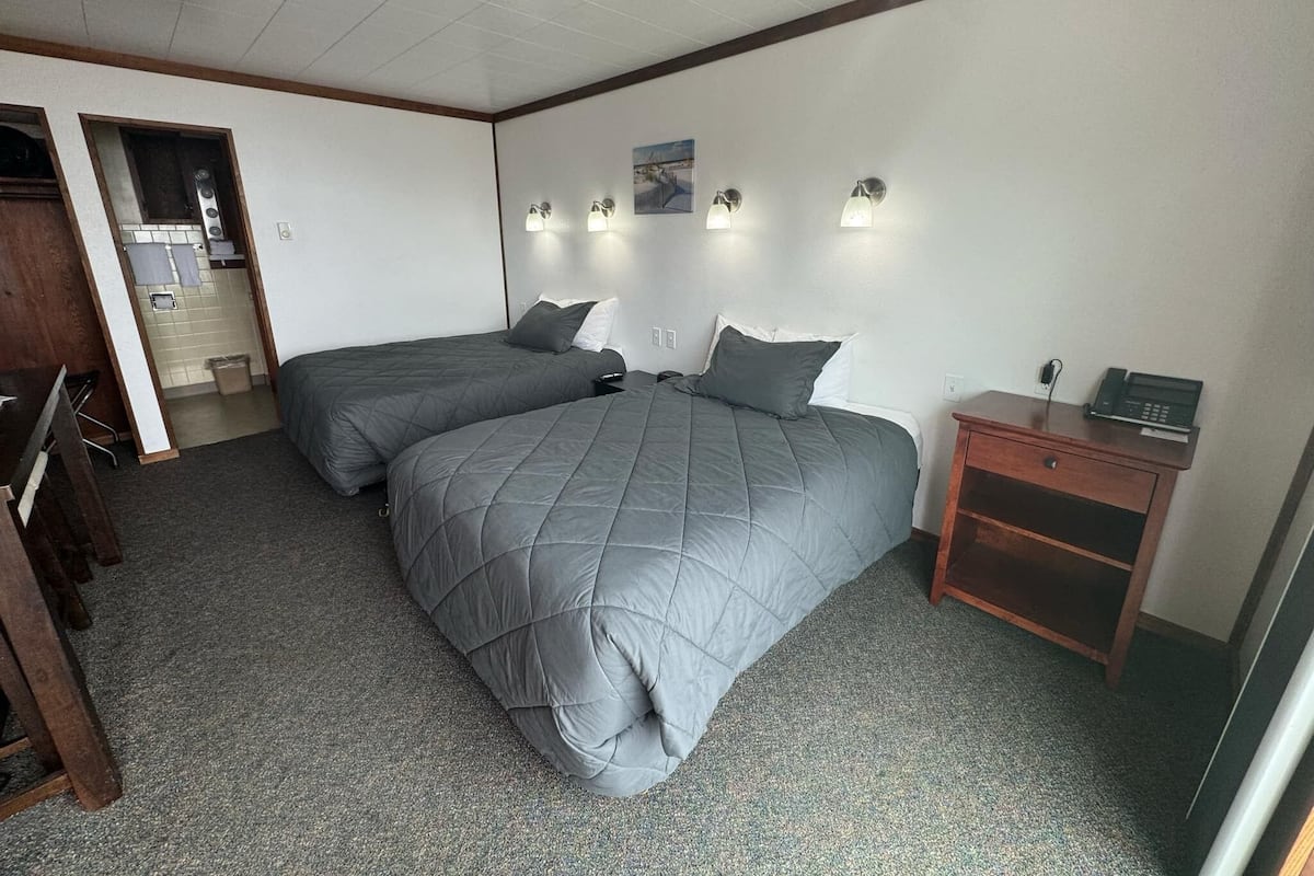A bedroom with two beds, a desk, a phone, and a small cabinet.