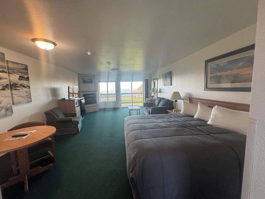 A hotel room with a bed, a desk, a chair, a small table, and a balcony with a view.