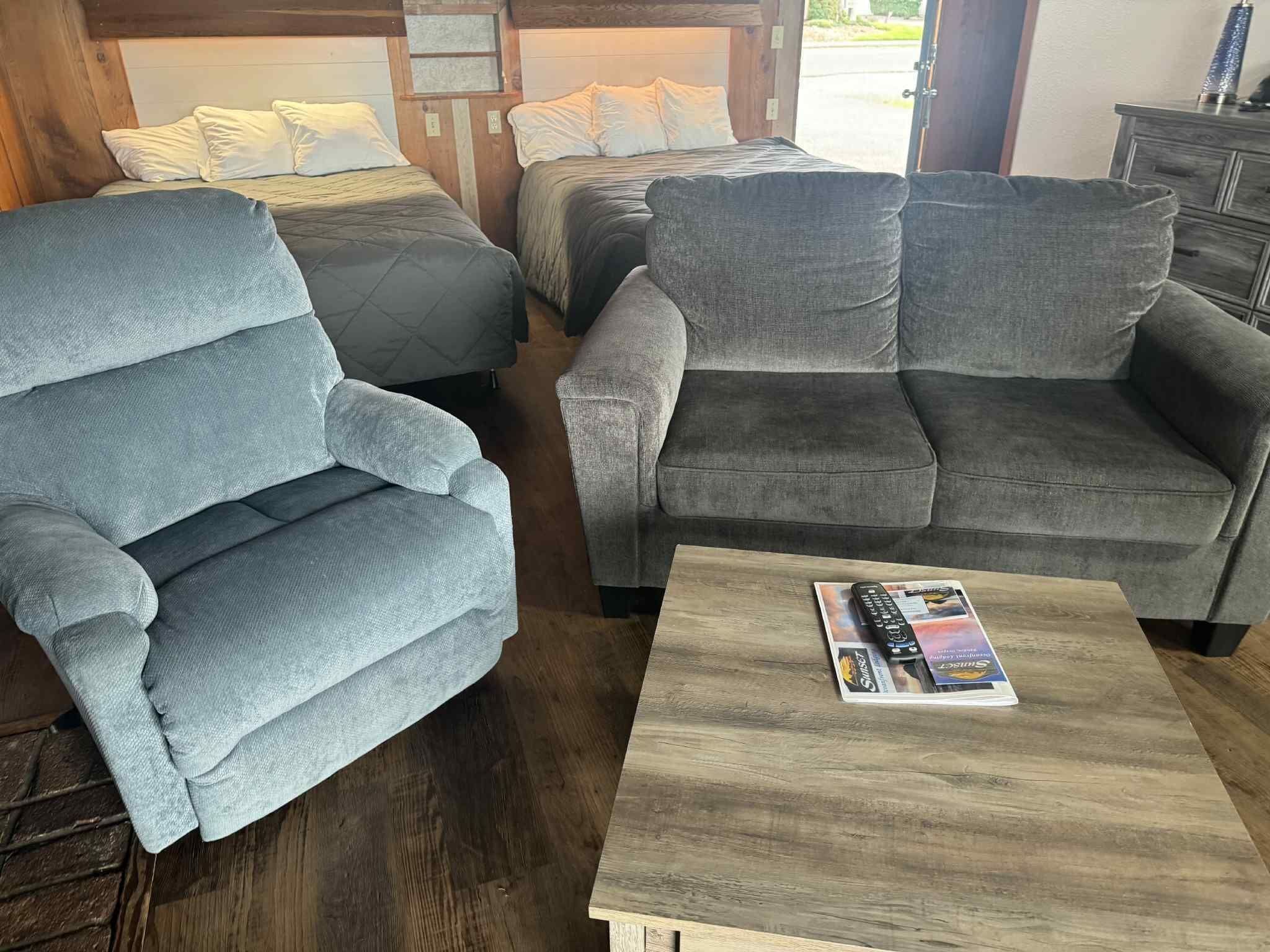 Una habitación acogedora con un sillón gris, un sofá gris y una mesa de centro de madera con una revista.