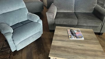 Una habitación acogedora con un sillón gris, un sofá gris y una mesa de centro de madera con una revista.