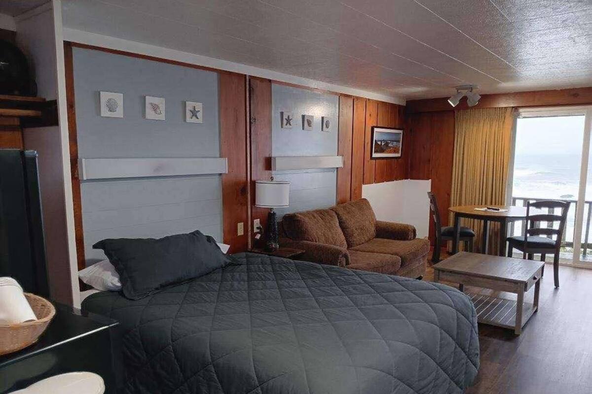 A room with a large bed, a sofa, a table, and a view of the ocean.