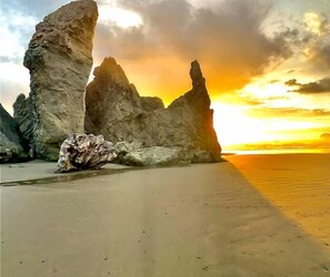A beach with large rock formations and a sunset. - Sunset Oceanfront Lodging (Bandon)