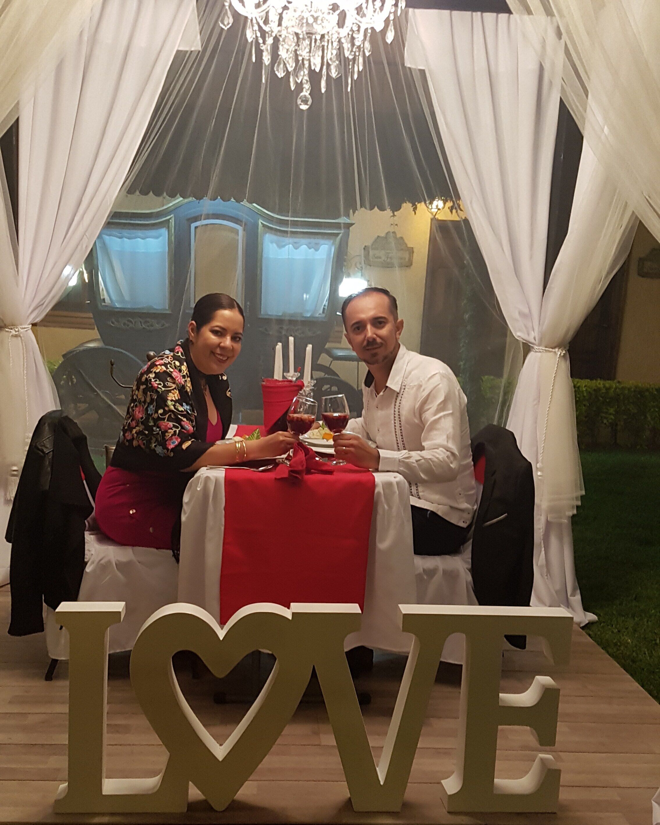 A wedding reception with a 'LOVE' sign centerpiece, white drapes, and a chandelier.