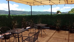 An outdoor patio with tables and chairs, surrounded by a hedge and a view of green hills. - Hotel Mision Colonial San Cristobal (San Cristóbal de las Casas)
