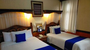 A hotel room with two beds, each with white bedding and blue accents. There is a nightstand with a phone and a wall-mounted light between the beds. - Hotel Mision Colonial San Cristobal (San Cristóbal de las Casas)