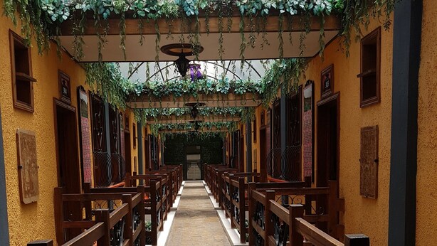A corridor with wooden benches and a stone floor, leading to a door at the end. - Hotel Mision Colonial San Cristobal (San Cristóbal de las Casas)