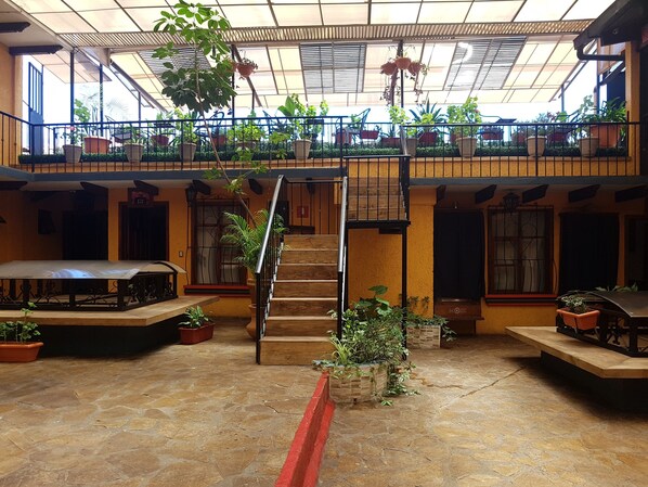 Un amplio atrio con una escalera central, varios niveles con balcones y numerosas plantas en macetas.