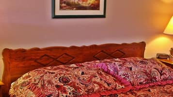 Una cama bien tendida con una colcha estampada, dos lámparas de noche, un cuadro enmarcado en la pared y una mesita de madera con un control remoto.