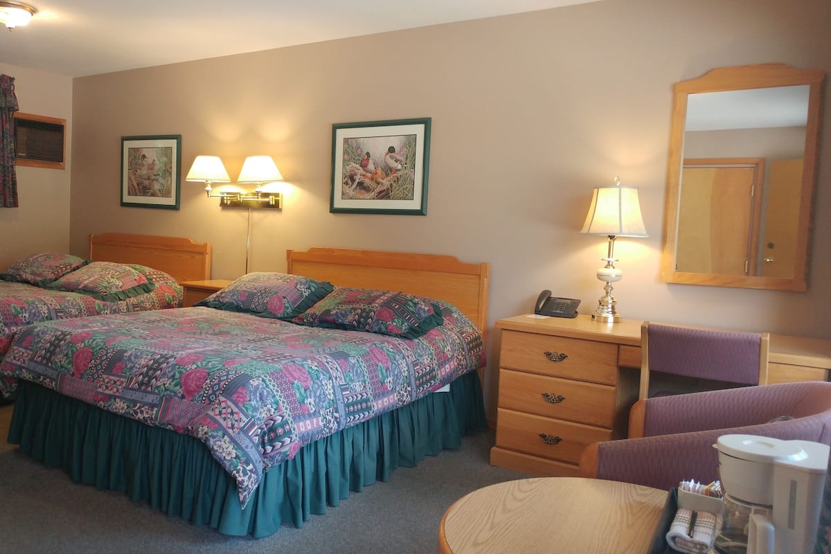 Una habitación de hotel con dos camas, un escritorio, una silla y un espejo.