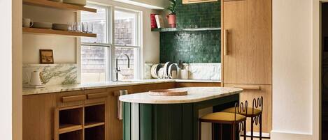 Una cocina con armarios de madera, encimera de mármol, una isla verde y dos taburetes de bar.
