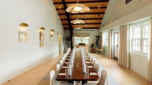 A long conference table with chairs, white walls, wooden ceiling beams, and framed pictures on the walls. - The Beachside (Nantucket)