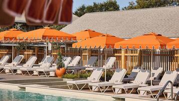A poolside area with lounge chairs and orange umbrellas, a tiled pool, and a wooden fence in the background.