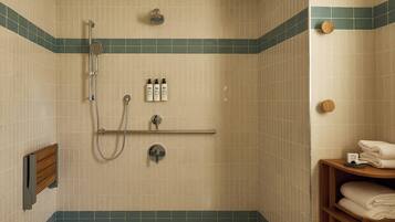 A small, tiled shower room with a showerhead, handheld shower, and a handheld shower attachment. There are three bottles of shampoo and conditioner on the wall, and a towel rack with folded towels.