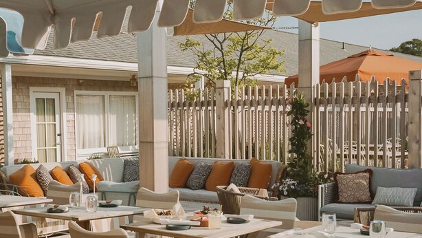 An outdoor seating area with tables and chairs, a covered patio, and a wooden fence in the background. - The Beachside (Nantucket)