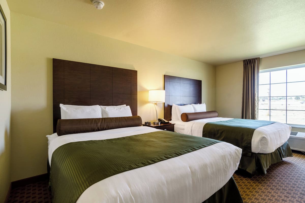 A hotel room with two beds, a nightstand with a lamp, and a window with curtains.