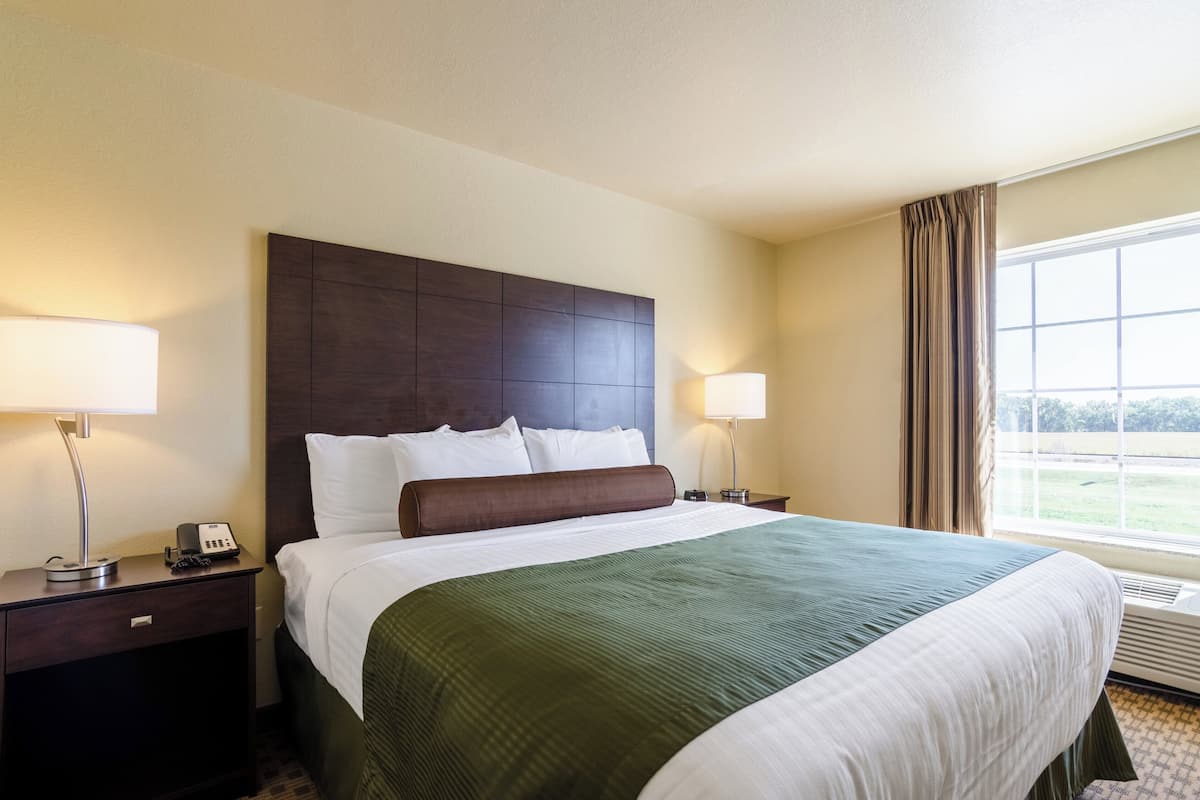 A hotel room with a large bed, two bedside lamps, a nightstand with a phone, and a window with curtains.
