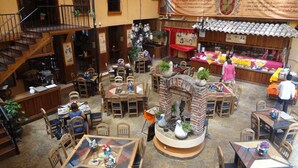 A spacious restaurant with multiple dining areas, a central brick fireplace, and a variety of seating options including tables and chairs. - Nuestras Raices - Hotel Museo Restaurante (San Cristóbal de las Casas)