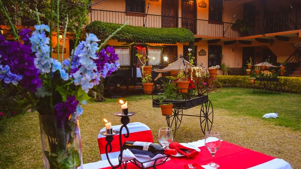 An outdoor dining area with a table set for two, surrounded by potted plants and a carriage. - Nuestras Raices - Hotel Museo Restaurante (San Cristóbal de las Casas)