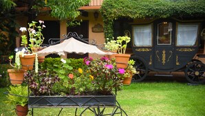 A garden cart with potted plants and flowers in front of a building with a carriage parked nearby. - Nuestras Raices - Hotel Museo Restaurante (San Cristóbal de las Casas)