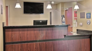 Una reception con scrivania, un laptop, lampade pendenti e un televisore a schermo piatto appeso al muro.