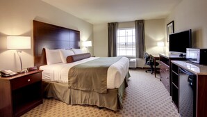 A hotel room with a large bed, a desk with a computer, a TV, and a window with curtains.