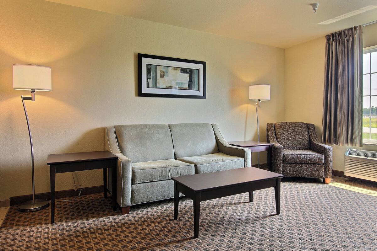 A hotel room with a sofa, armchair, and a small table. There are two wall-mounted lamps and a framed picture on the wall.