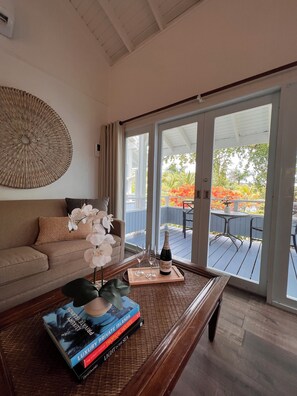 A living room with a sofa, a coffee table with books and a bottle, and a view of an outdoor deck with chairs and a table. - Club Seabourne Boutique Hotel (Culebra)