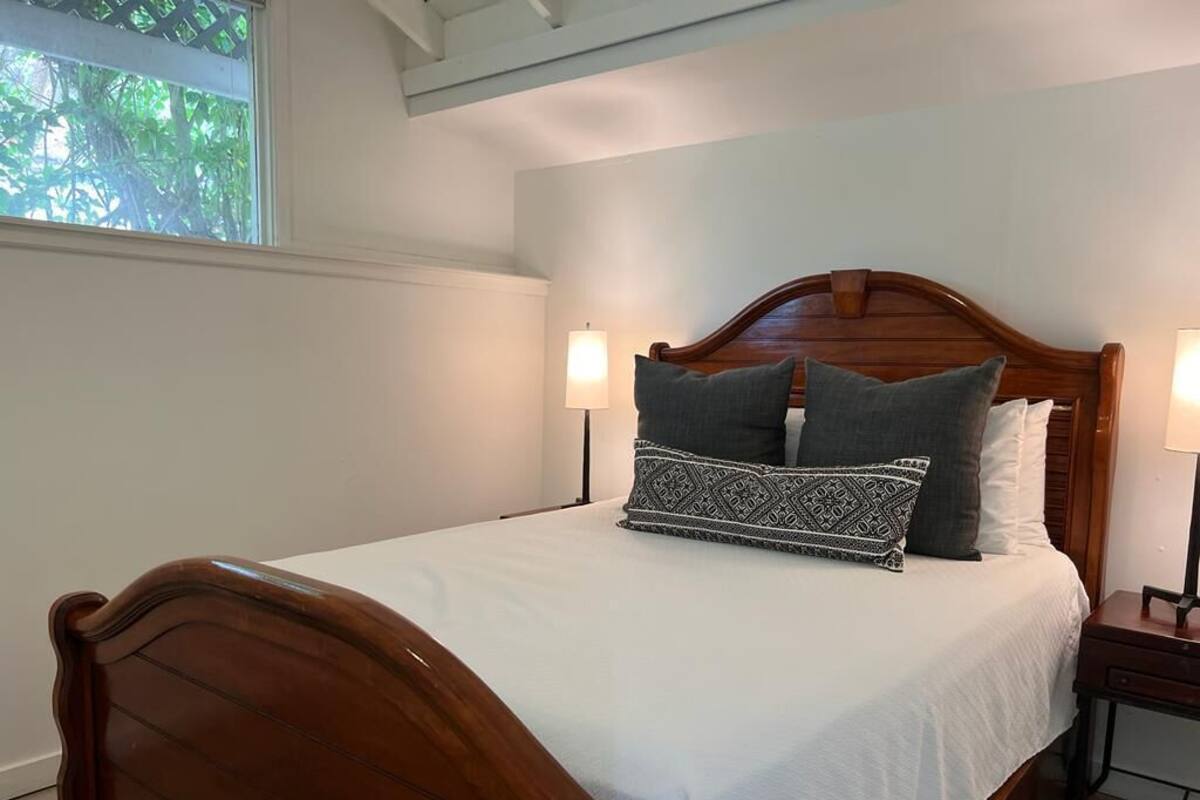 A neatly made bed with a wooden headboard, two bedside lamps, and a patterned pillow.