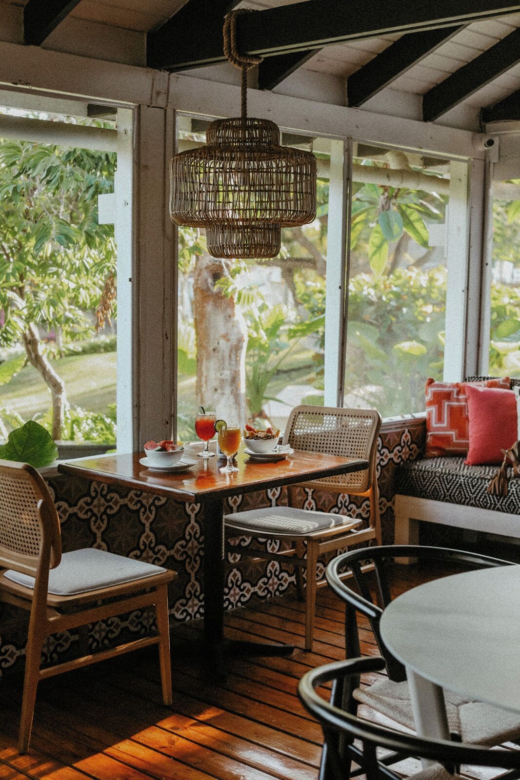 A cozy outdoor seating area with wicker chairs and a table, surrounded by large windows offering a view of greenery.