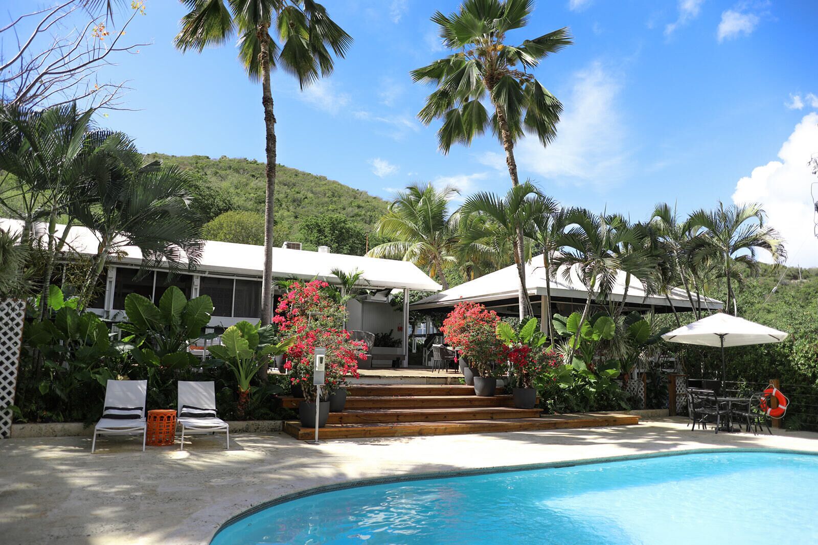 A pool area with a clear blue pool, surrounded by palm trees and a building with a white roof.