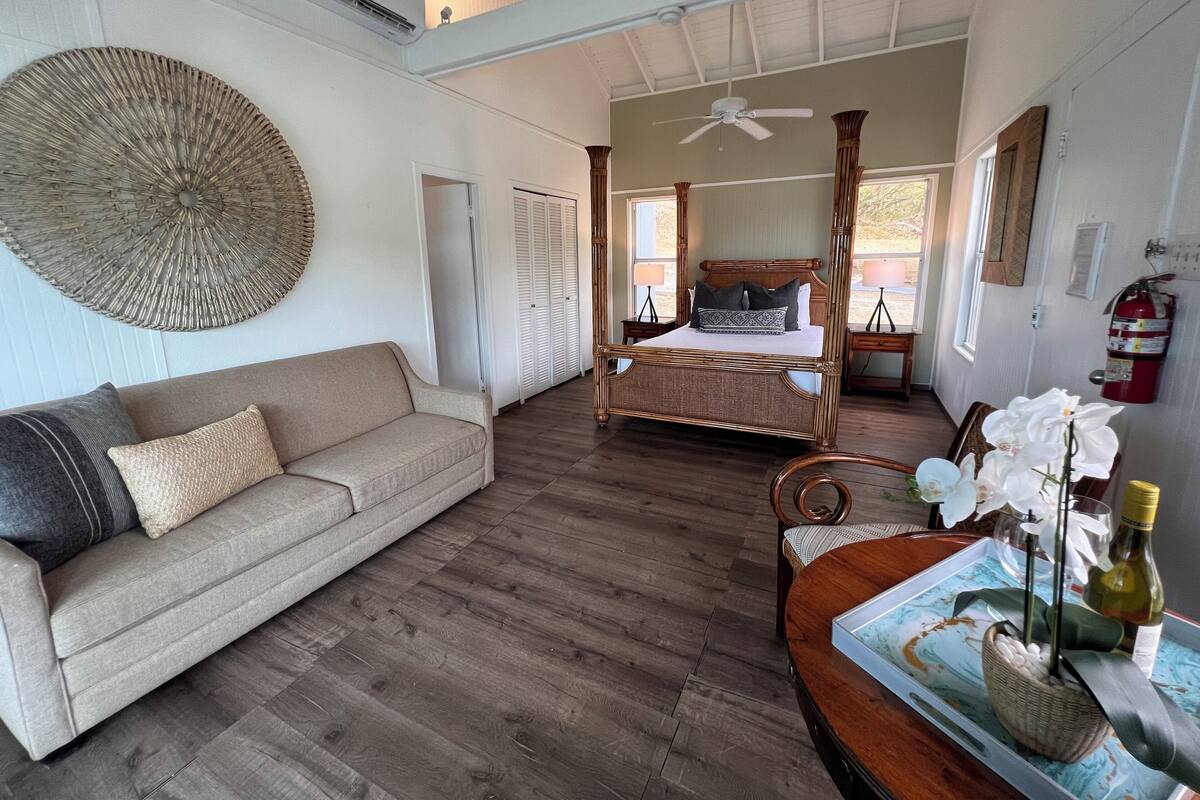 A spacious room with a large bed, a sofa, a ceiling fan, and a decorative wall hanging.