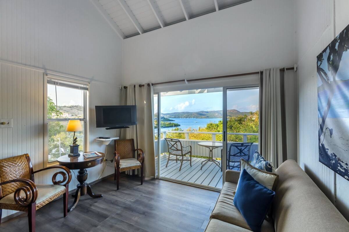 A spacious living room with a balcony, a television, and a view of the sea.