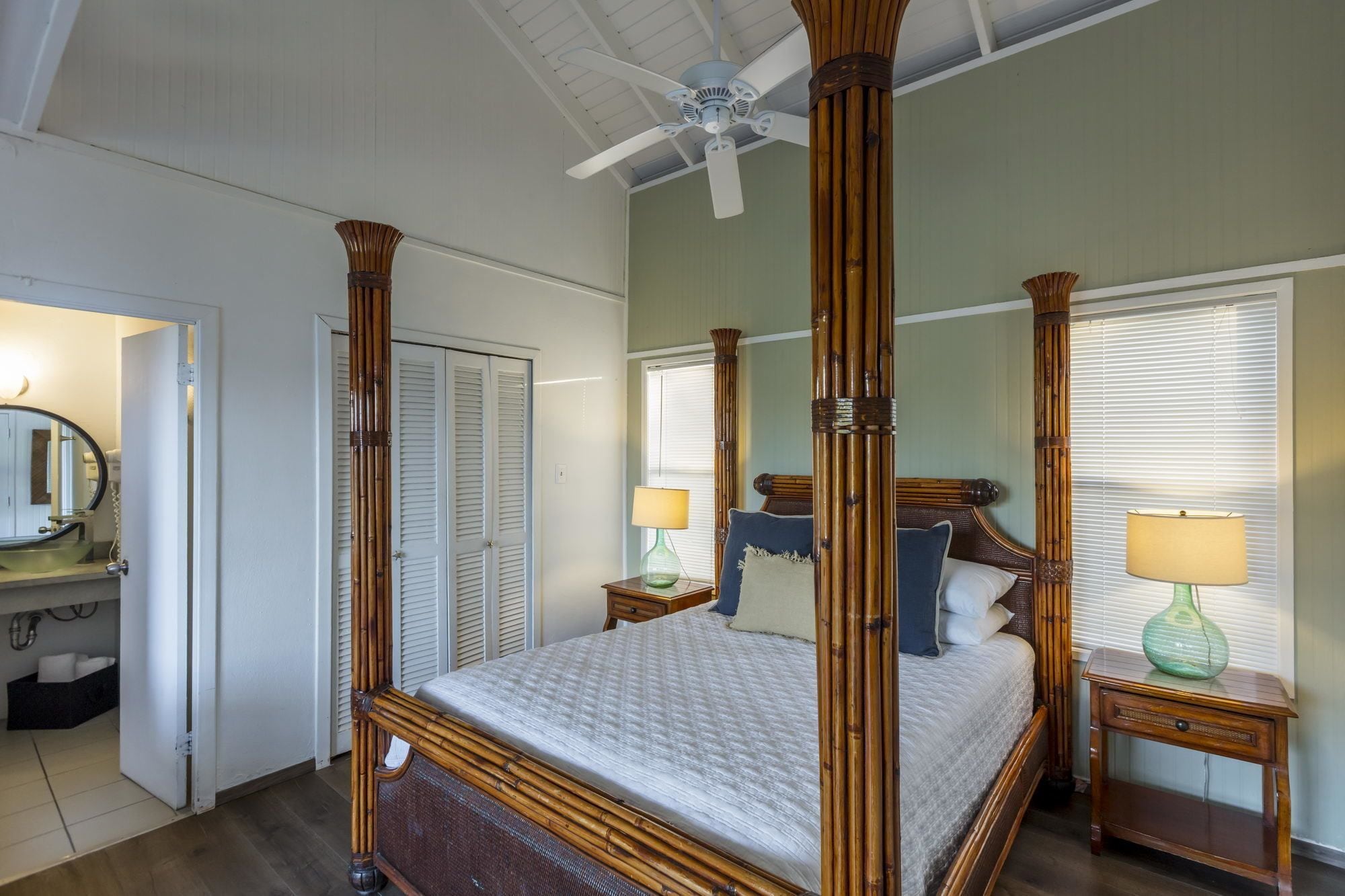 Un lit à baldaquin avec un cadre en bois, un ventilateur de plafond et une table de chevet avec une lampe.