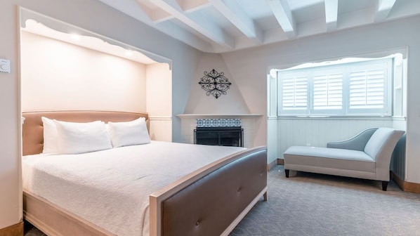 Un dormitorio con cama, sofá, chimenea y ventana con contraventanas.